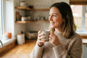 Smiling woman in a cozy kitchen holding a steaming mug, enjoying hot water from ARNO tap